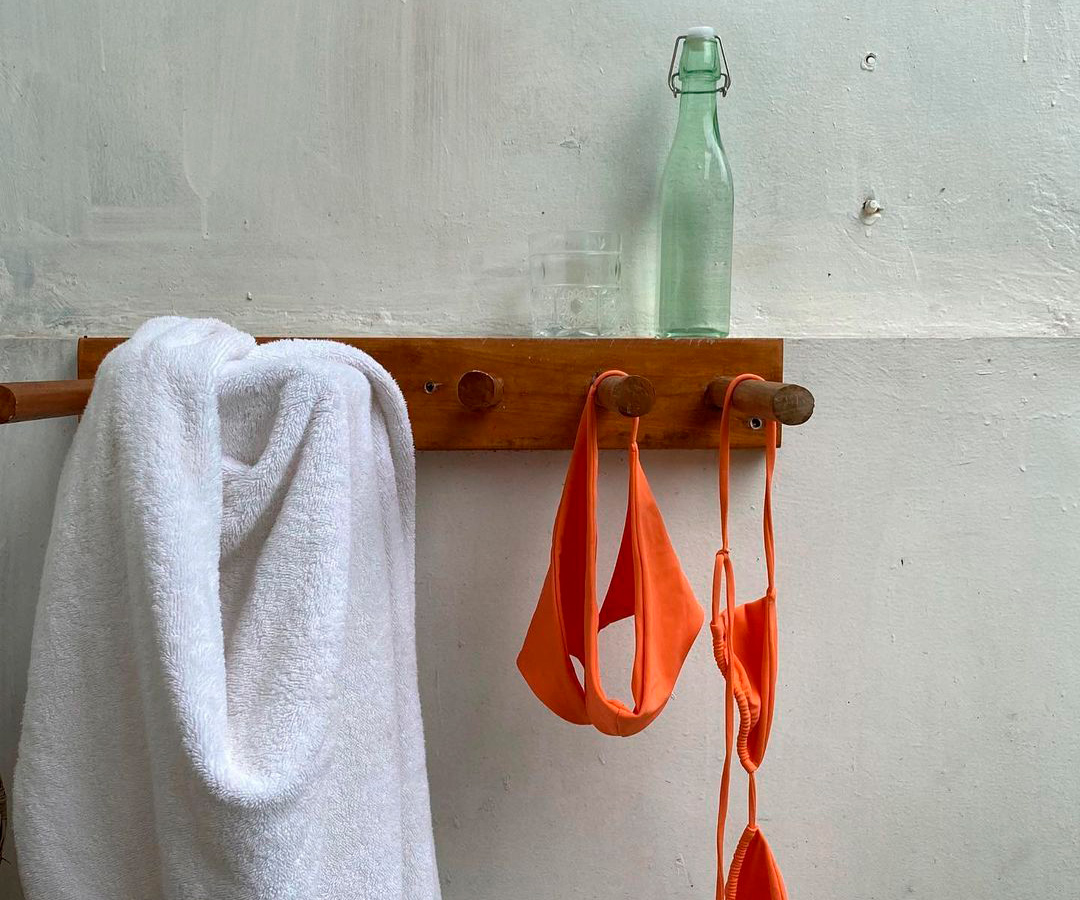 Bikini and towel hanging on rack with a water on top.
